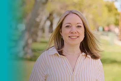 Person standing outdoors in a park with trees and grass in the background